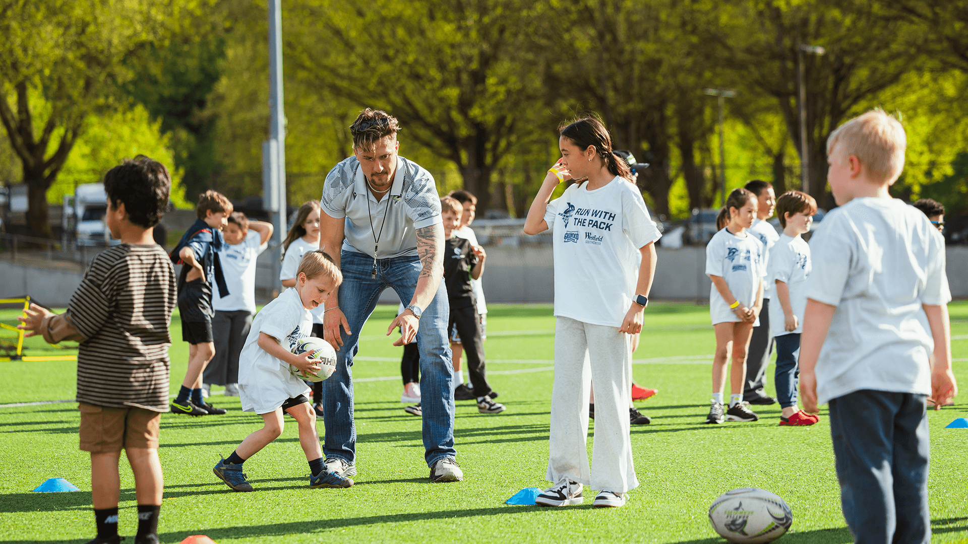 Seawolves coaches lead young players through a rugby clinic on a grass field