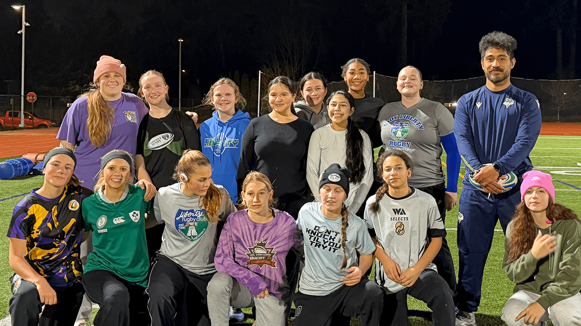 Women's rugby players pose for a team photo with a Seawolves coach under the lights